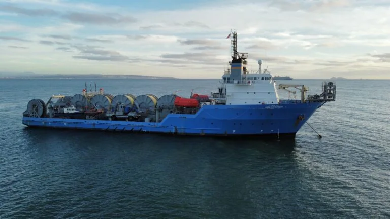 Oil supply ship with large tanks and equipment on deck, floating on calm water under a cloudy sky.