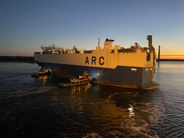 ARC ship Patria at sunset with tugboats assisting.
