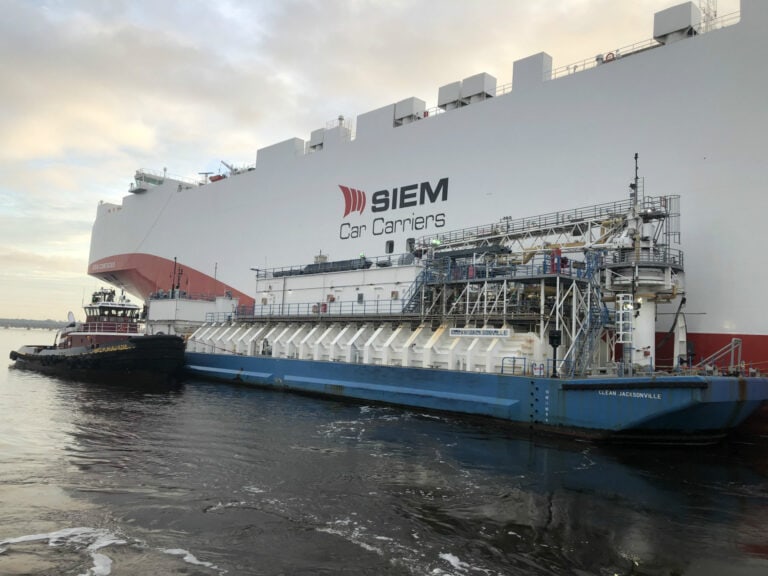 SIEM Car Carriers ship docked at port with tugboats nearby.
