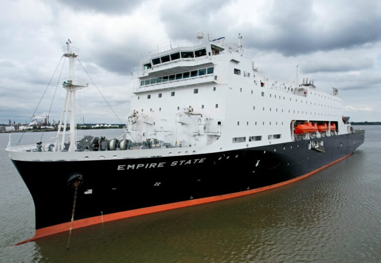 Large white and black ship named Empire State docked on water.