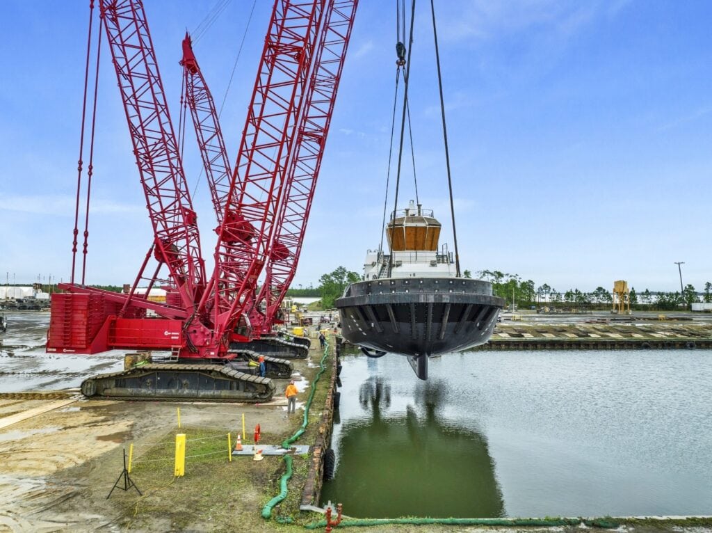 Large red crane lifting a boat over water at a construction site.