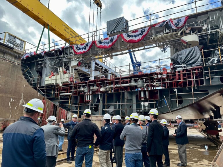 Group of people in safety helmets inspecting a large ship at a shipyard.