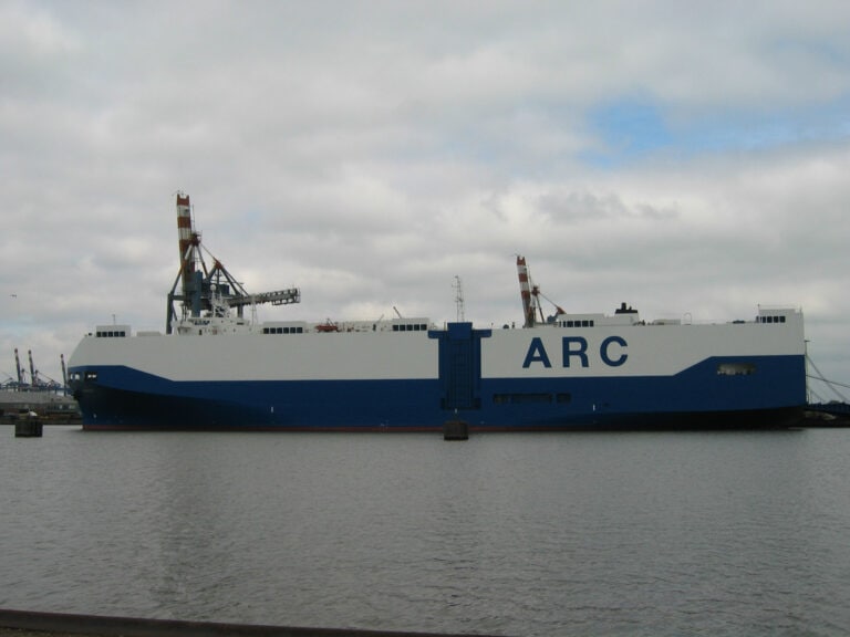 Large cargo ship with 'ARC' written on the side, docked at port under cloudy sky.