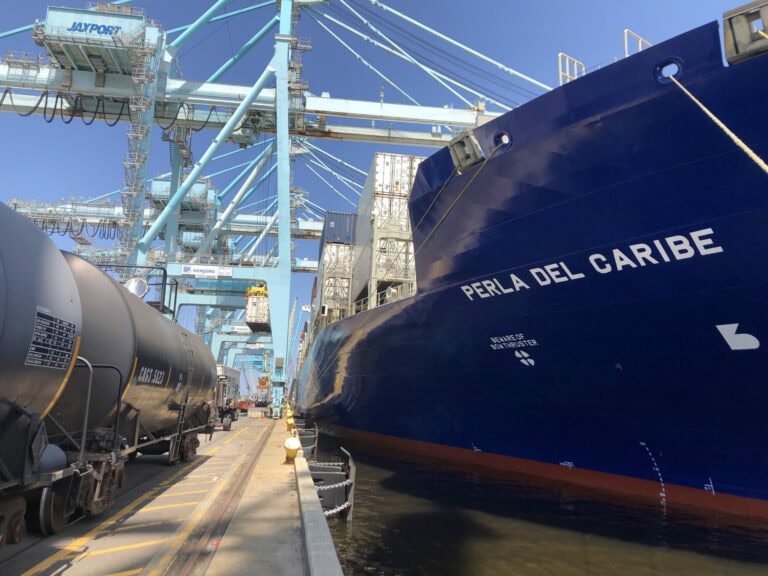 Cargo ship "Perla del Caribe" docked at port with cranes overhead.