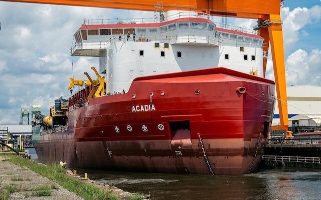 Large red and white ship named 'ACADIA' docked at a port with a yellow crane overhead.