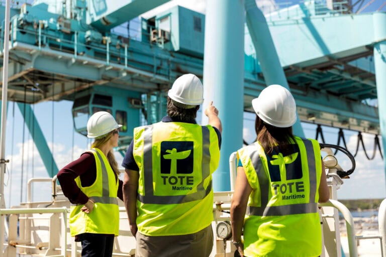 Three maritime workers in safety vests and helmets on an offshore platform.