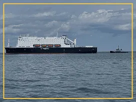 Large cargo ship with containers on the water, with a tugboat nearby.