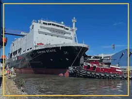Large white and black ship docked at a port with a red tugboat nearby.
