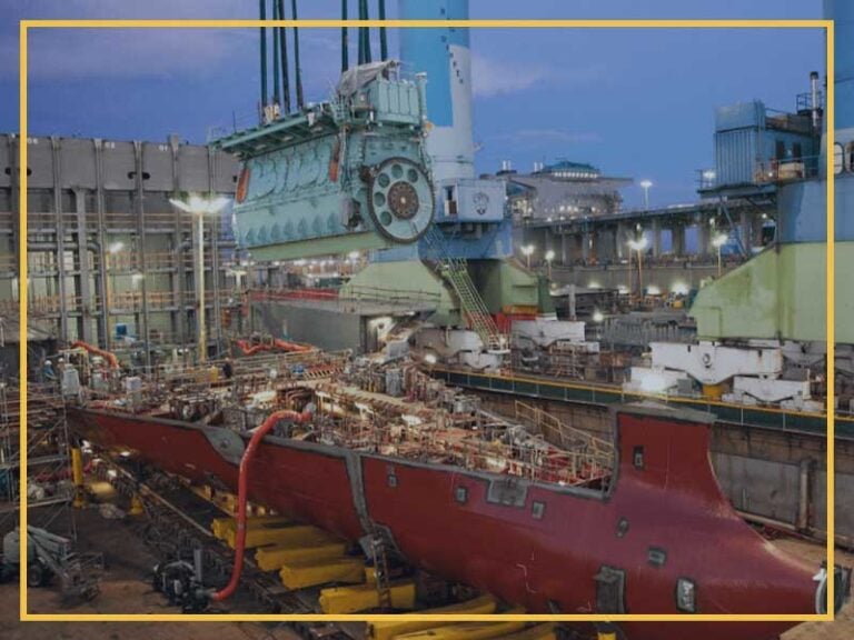 Large ship hull being constructed in a shipyard at dusk.