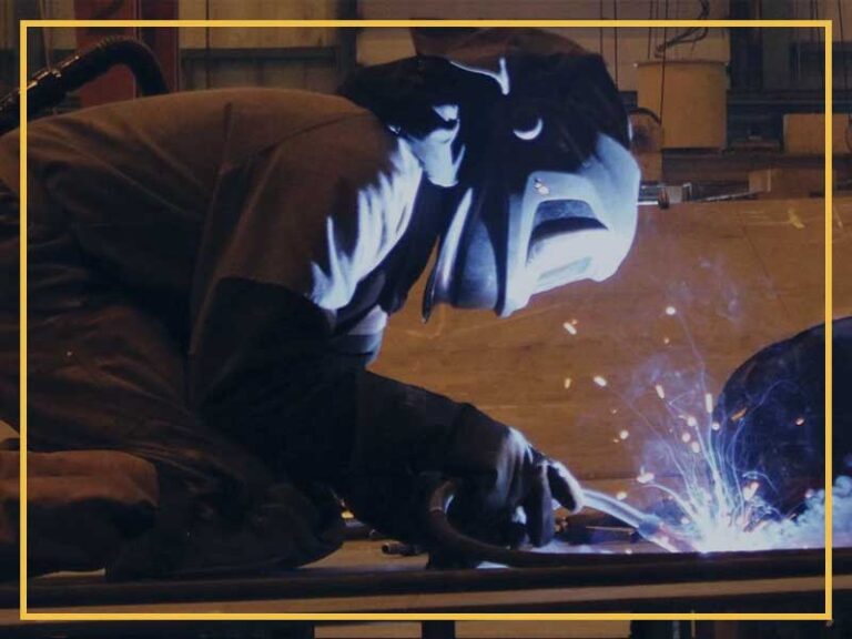 Welding worker in safety gear welding metal on ship construction site.