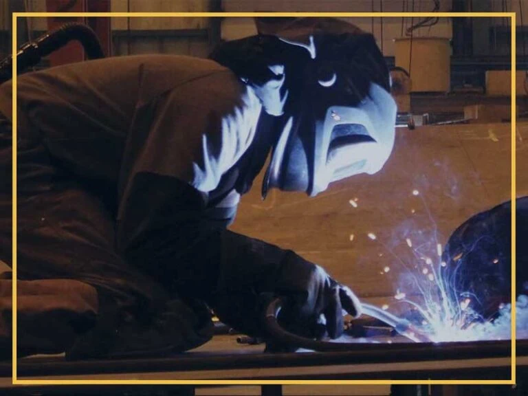 Welding worker in safety gear welding metal on ship construction site.