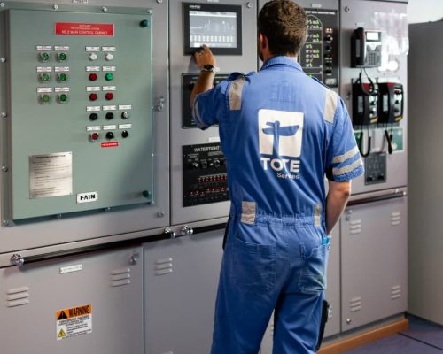 16-print-2100-kitty-hawk-ave – TOTE Services Technician operating control panel in industrial setting.