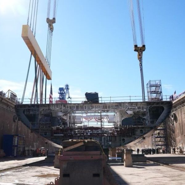 Large ship under construction in a dry dock with cranes overhead.