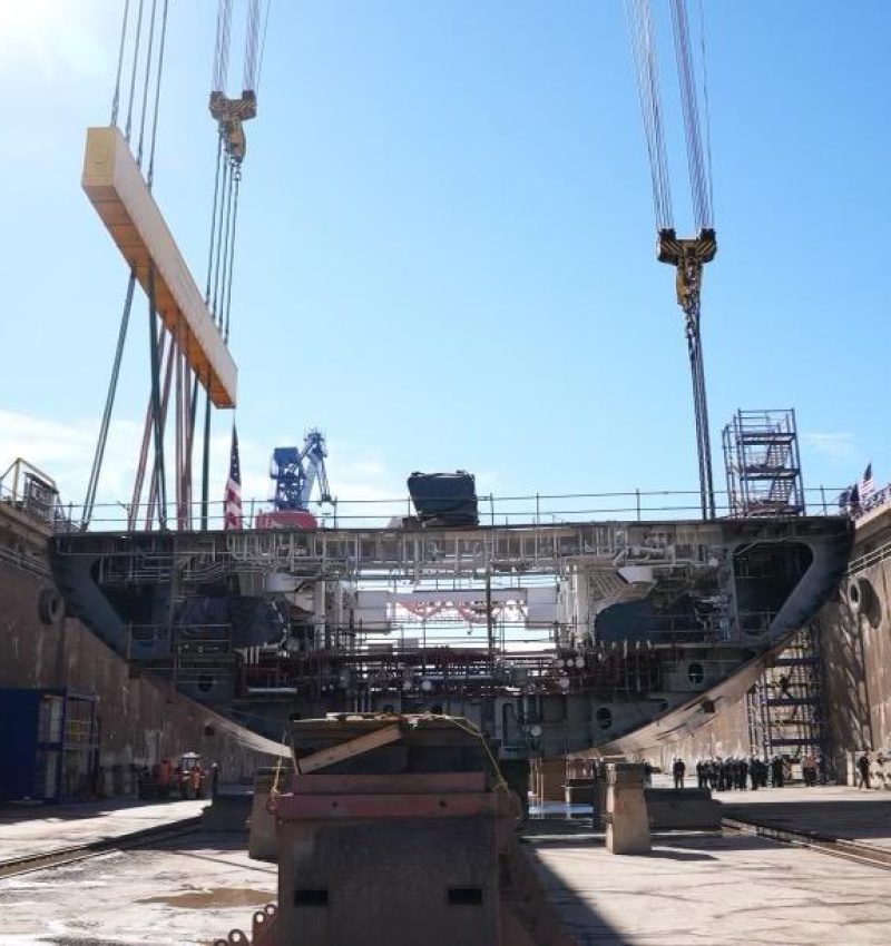 Large ship under construction in a dry dock with cranes overhead.