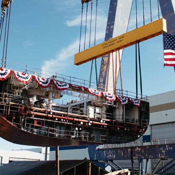 Ship being lifted by a large crane with American flag decorations.