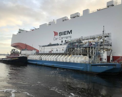 SIEM Car Carriers ship docked at port with tugboats nearby.