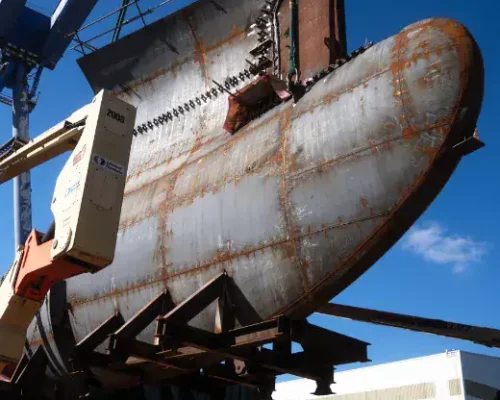 Feb-2024 Large rusty submarine hull being lifted by crane at a dockyard.