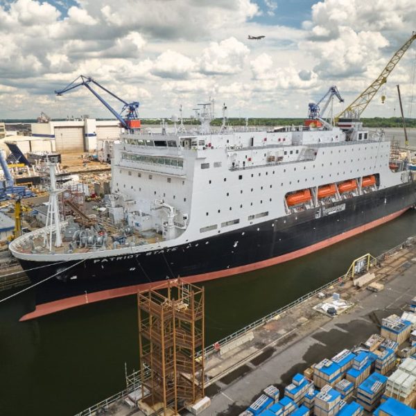 Large ship in dry dock with cranes and containers nearby.