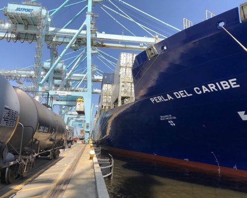 Cargo ship "Perla del Caribe" docked at port with cranes overhead.