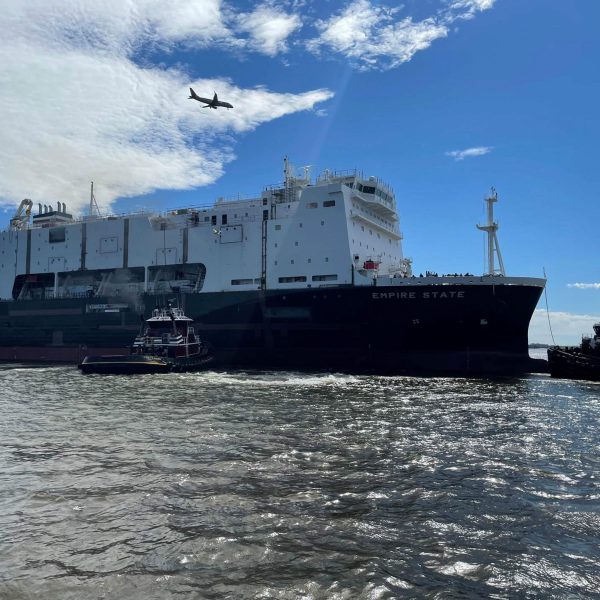 Large cargo ship named Empire State docked at port with smaller boats nearby.