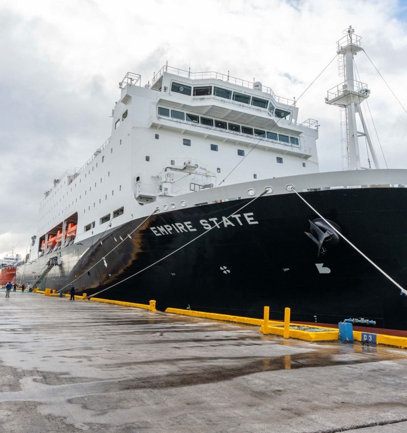 Empire State cruise ship docked at the port, with a cloudy sky overhead.