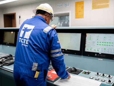 emissions control Worker in blue uniform and helmet operating control panel at TOTE Services.