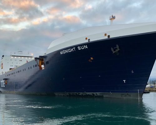 Large cruise ship named MIDNIGHT SUN docked at port with cloudy sky.